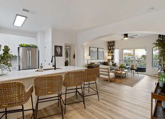 the kitchen and living room of a house with a large white counter and bar chairs