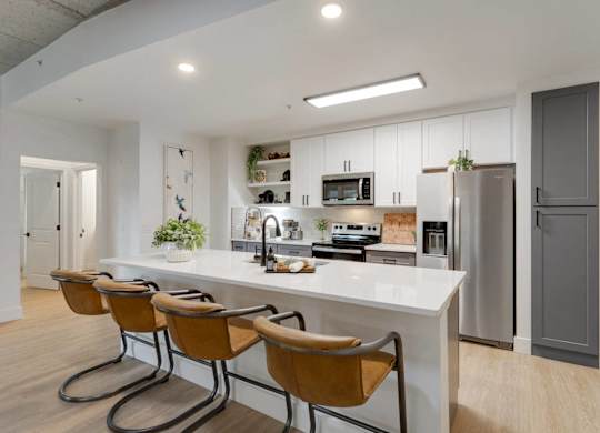 A modern kitchen with a white countertop and brown chairs.