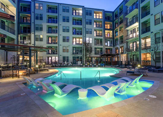 A swimming pool in front of apartment buildings at dusk.