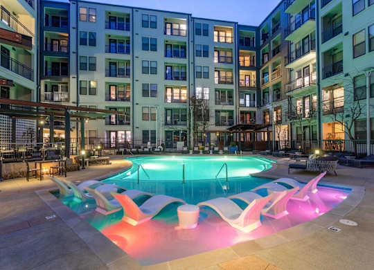 A swimming pool in front of apartment buildings at dusk.