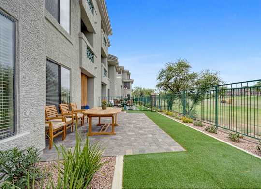 A patio with a table and chairs is surrounded by a green fence.