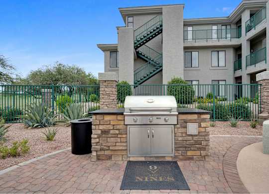 an outdoor kitchen with a grill and a trash can in front of an apartment building