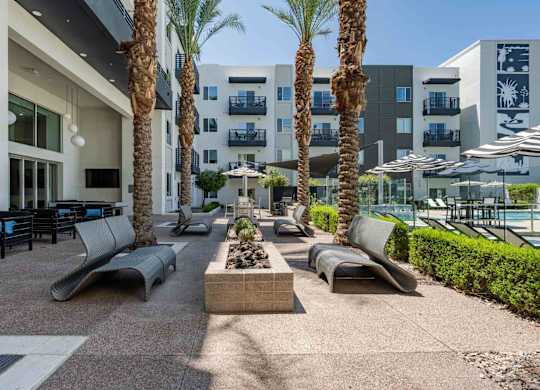a patio with lounge chairs and a fire pit in front of a slate scottsdale apartment building