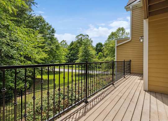 A balcony with a black railing overlooks a green lawn and trees.
