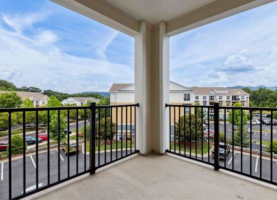 A balcony overlooks a parking lot and buildings.