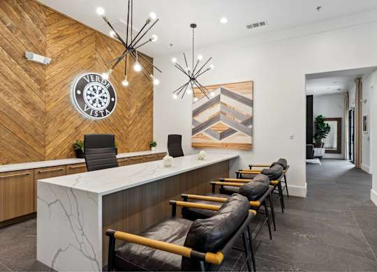 A reception area with a white counter and black chairs.