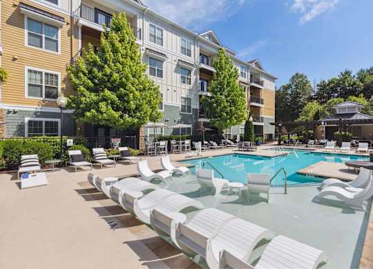 A large swimming pool surrounded by sun loungers and trees.