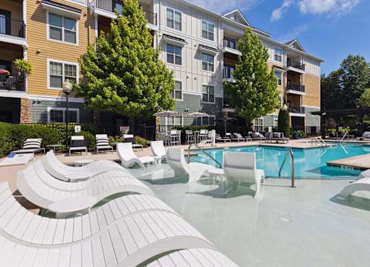 A large swimming pool with sun loungers in front of apartment buildings.
