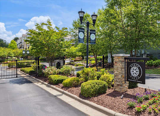 A black and white sign with a dartboard design is mounted on a stone pillar at the entrance to a gated community.
