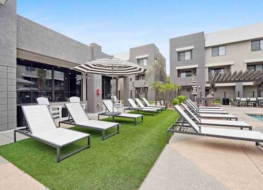 A row of sun loungers are on a lawn in front of a building.