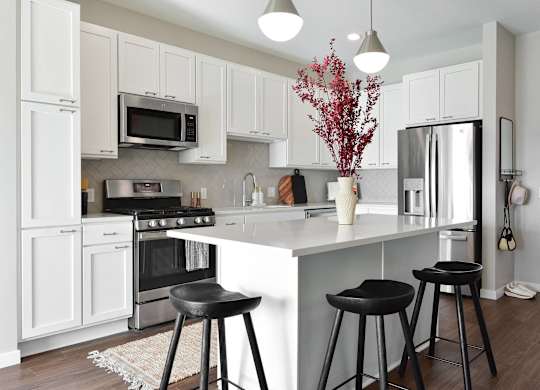 a kitchen with white cabinets and a white island with black stools at The Hallon Apartments, Hopkins, Minnesota