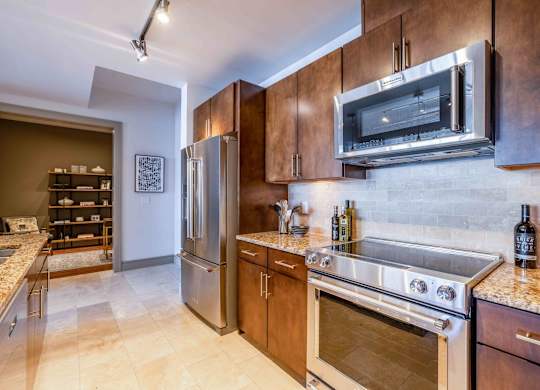 A kitchen with a stainless steel refrigerator and oven, wooden cabinets, and a marble countertop.