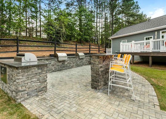 A stone patio with a white chair and a grill.