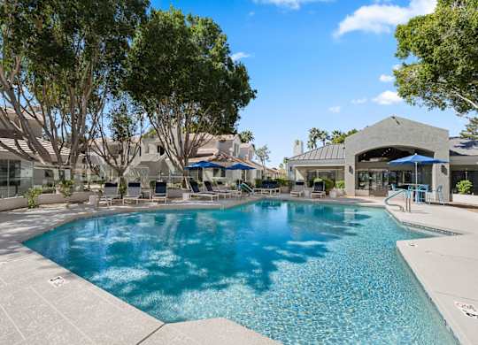 A large swimming pool surrounded by trees and a building in the background.