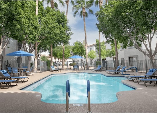 A pool surrounded by trees and chairs.