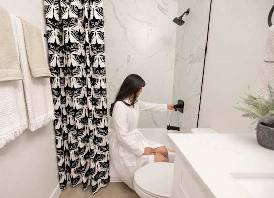 A woman in a white robe is sitting on a toilet in a bathroom.