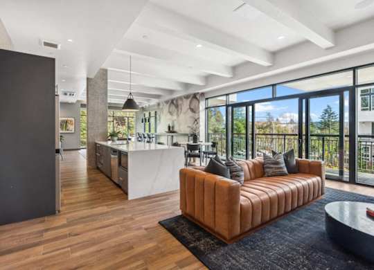 A modern living room with a brown leather sofa and a kitchen in the background.