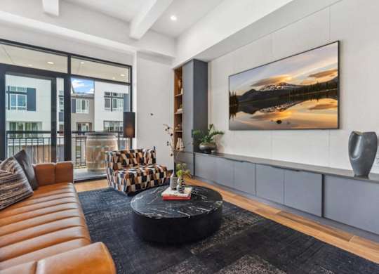 A modern living room with a large painting on the wall and a black coffee table in the center.