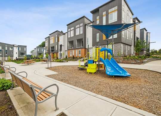 A playground with a blue slide and a bench in front of apartment buildings.