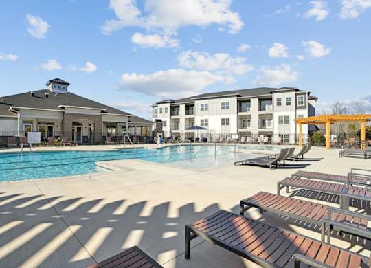 A sunny day at the pool with lounge chairs and apartment buildings in the background.