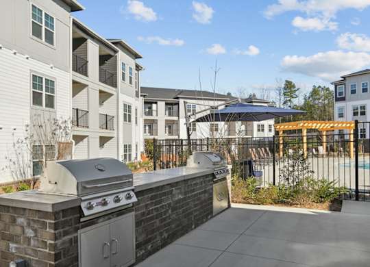 A BBQ grill is on a patio in front of apartment buildings.