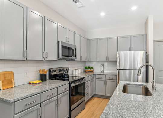 A kitchen with grey cabinets and a granite countertop.