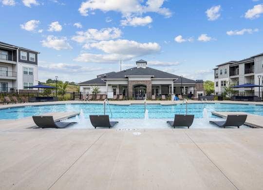 A large swimming pool with lounge chairs and a building in the background.