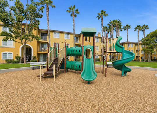 A playground with a green slide and a brown sandy ground.