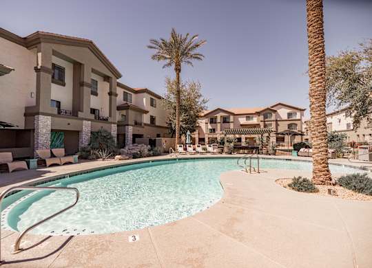 A pool surrounded by apartment buildings and palm trees.