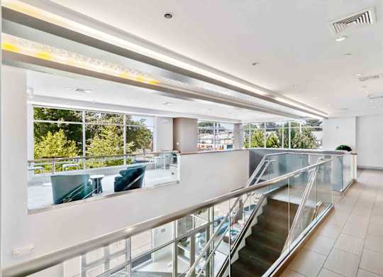 A staircase with a glass railing leads to a balcony with a view of trees.
