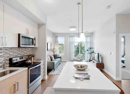 A modern kitchen with a white island and a dining area with a view.