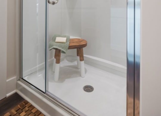 a shower with a glass door and a wooden stool