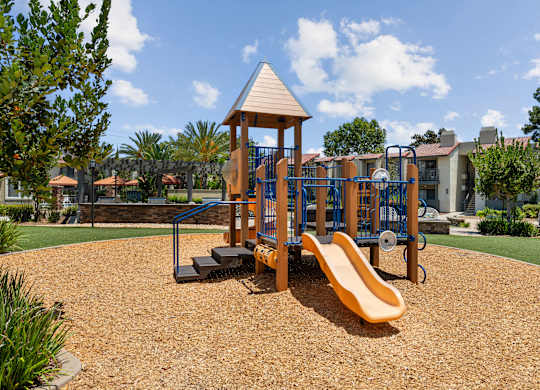 A playground with a yellow slide and a wooden structure.