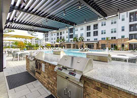 A barbecue grill is on a patio with a pool table and a building in the background.