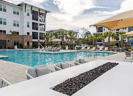 A large swimming pool with lounge chairs and a black rock border.
