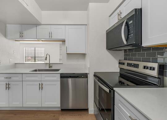 A kitchen with white cabinets and a black microwave.