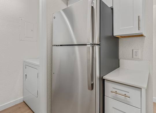 A stainless steel refrigerator stands in a kitchen with white cabinets and a white countertop.