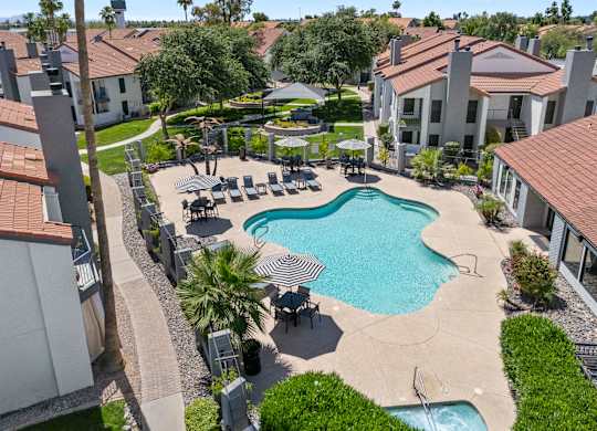 A swimming pool surrounded by a patio with chairs and umbrellas.