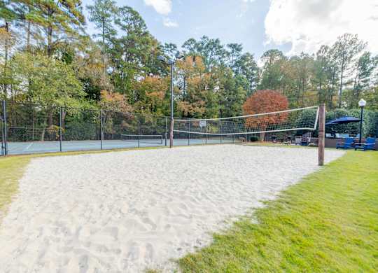 A sandy volleyball court surrounded by a fence and trees.