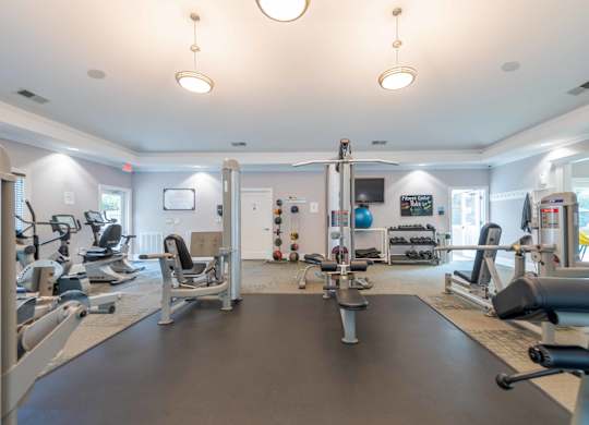 A spacious gym with various exercise equipment and a large mirror on the wall.