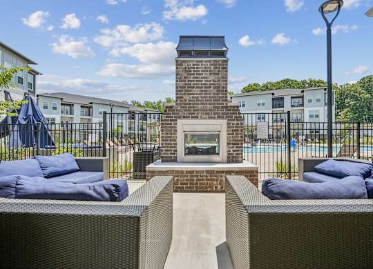 A patio with a fireplace and cushions is surrounded by a fence.