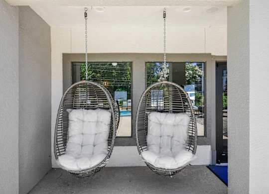 Two white hanging chairs with cushions are suspended from the ceiling in a room.