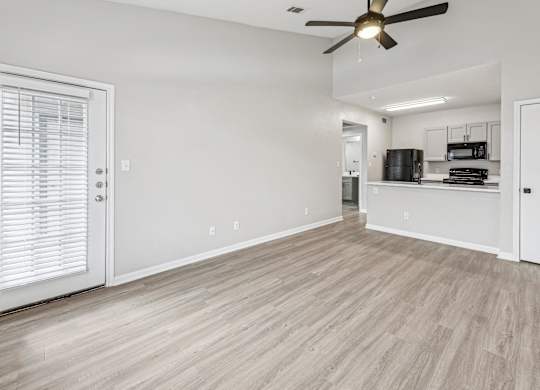 A room with a ceiling fan and light, a door with blinds, and a kitchenette in the background at Clear Creek Meadows Apartments, Copperas Cove, 76522