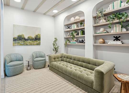A living room with a green couch, two chairs, and a painting on the wall.