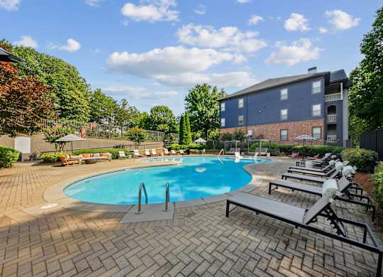 A swimming pool surrounded by a brick patio and lounge chairs.