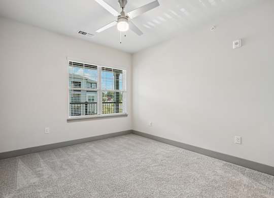 A room with a ceiling fan and a window overlooking a building.