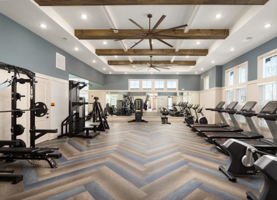 a gym with cardio machines and windows and a ceiling fan