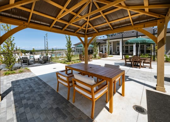 a patio with a wooden table and chairs under a wooden gazebo