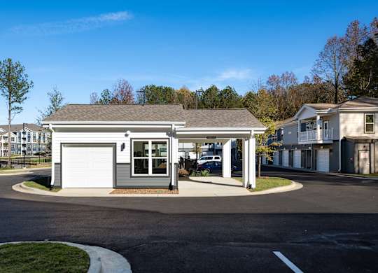 A small building with a grey roof and a white garage door is surrounded by a parking lot.