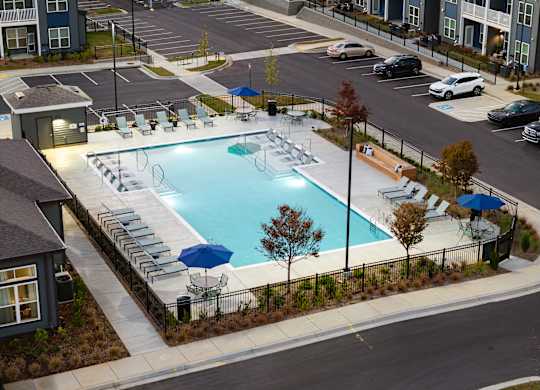 A swimming pool surrounded by chairs and umbrellas in a parking lot.